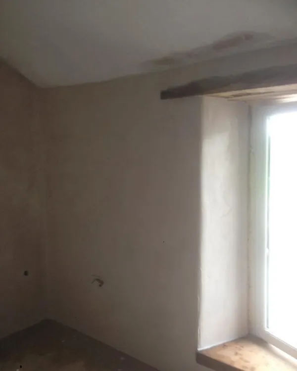 Freshly plastered room with a deep window reveal under a timber lintel and a sloping ceiling