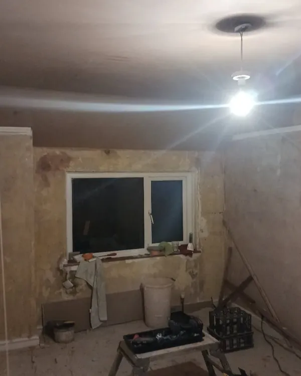 Bedroom with a new ceiling and pendant light, the walls still showing old patched plaster, and a window
