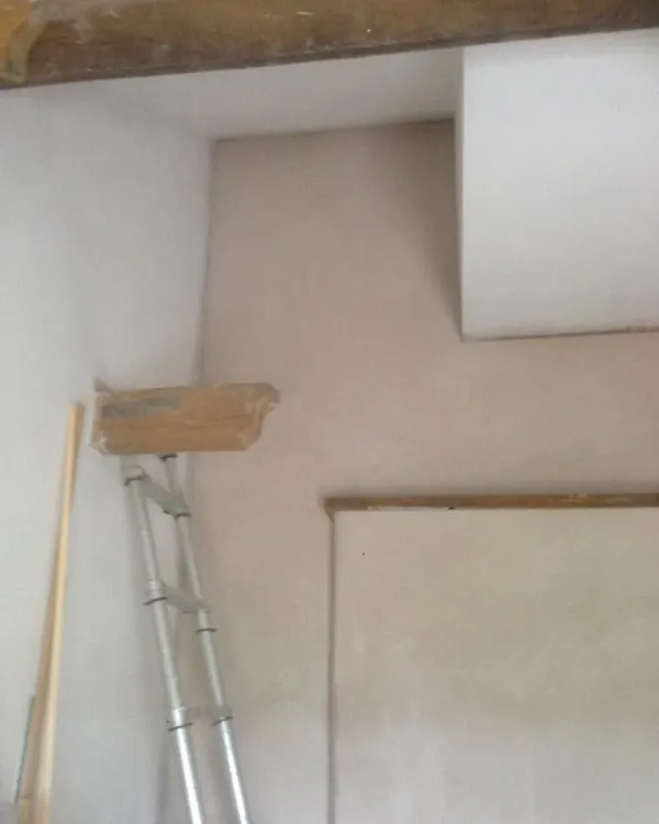 Freshly plastered cottage walls below an old timber beam, with a timber lintel and a ladder