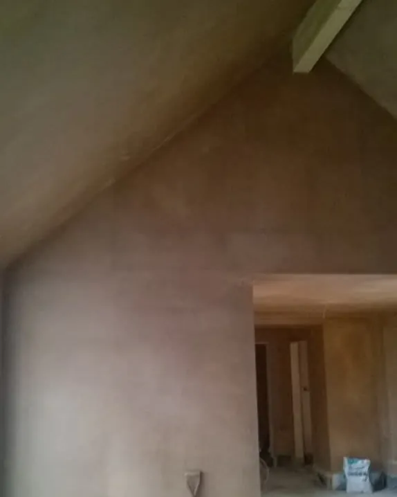 Tall gable wall and sloping ceiling with fresh pink plaster, a spade leaning against the wall