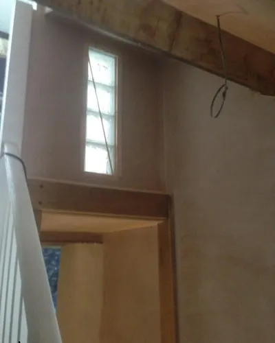 Plastered stairwell with a narrow glass-block window, an exposed beam and a timber door lining beside the banister