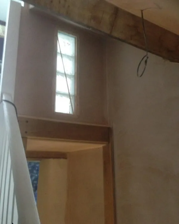 Plastered stairwell with a narrow glass-block window, an exposed beam and a timber door lining beside the banister