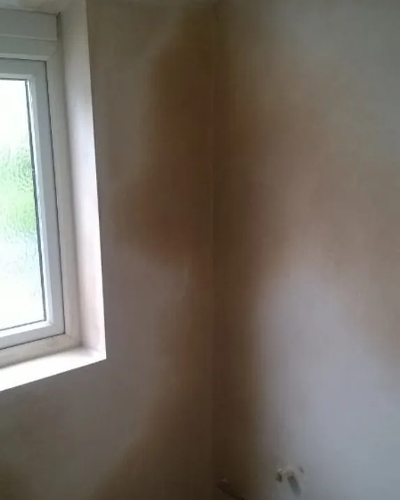 Freshly plastered corner beside a white window, with darker patches where the plaster is still drying