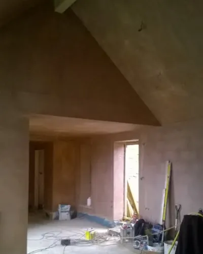 Freshly plastered room with a vaulted ceiling and a wide opening through to the next room, tools on the concrete floor
