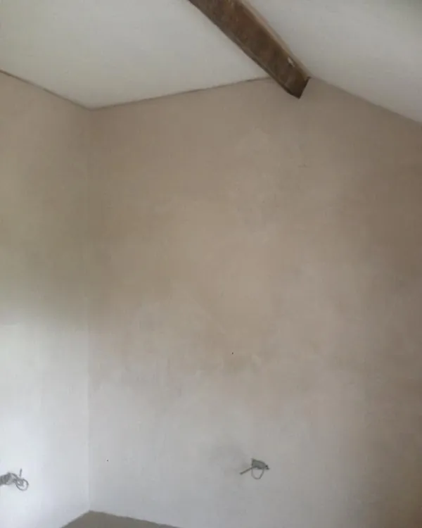 Corner of a room with smooth fresh plaster on the walls and an exposed timber beam across the ceiling