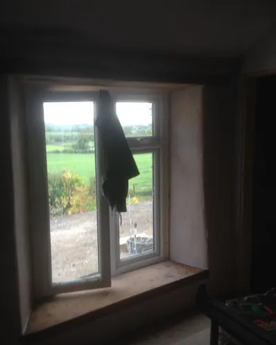 Plastered window reveal and timber sill in a thick wall, with fields visible through the window
